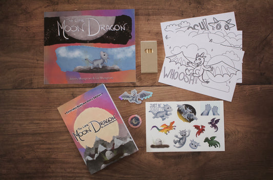 A children's dragon-themed activity set arranged on a wooden tabletop, including a book titled 'The Light Moon Dragon’, colouring pages, a sticker sheet, and individual stickers. 