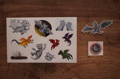 A sheet of dragon-themed stickers displayed on a wooden surface, alongside two individual stickers.